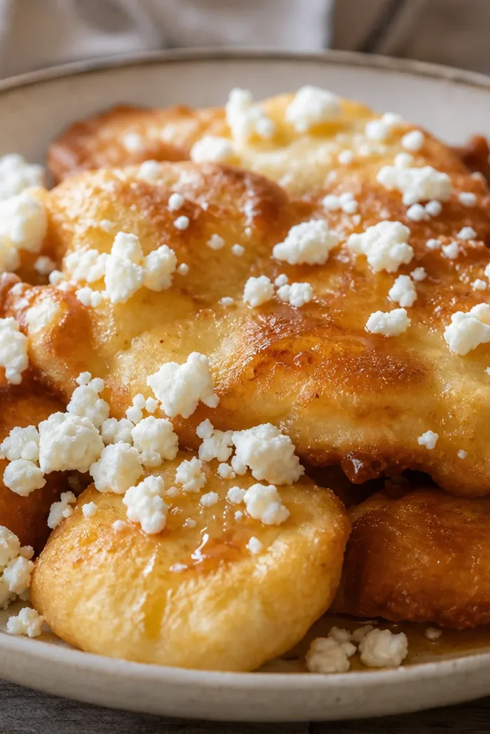 Golden-brown fried dough topped with honey and crumbled cheese, garnished with herbs.