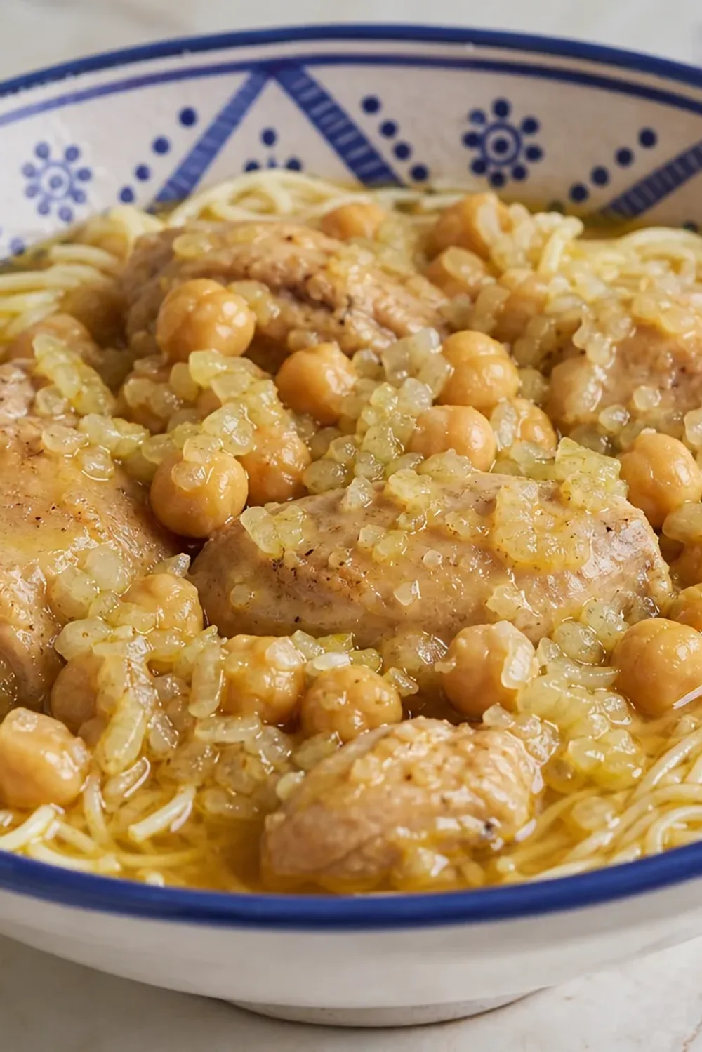 Plate of Algerian Rechta noodles with chicken, chickpeas, and herbs garnished with spices.