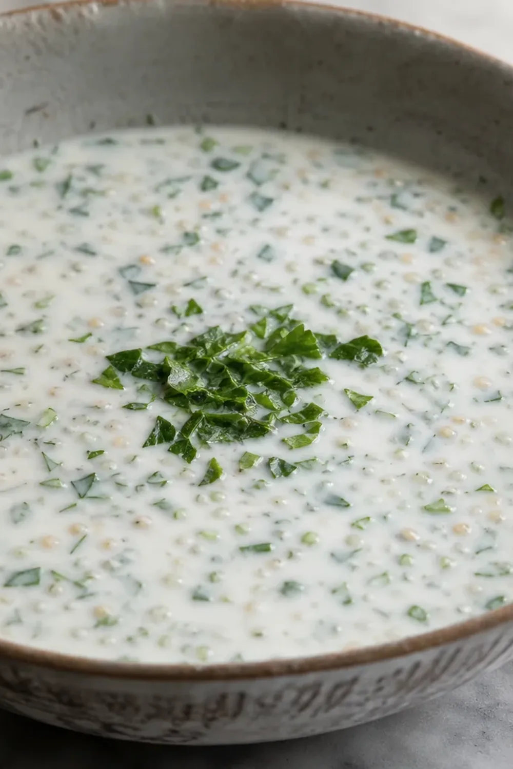 Creamy yogurt soup garnished with fresh herbs and wheat, served in a bowl.