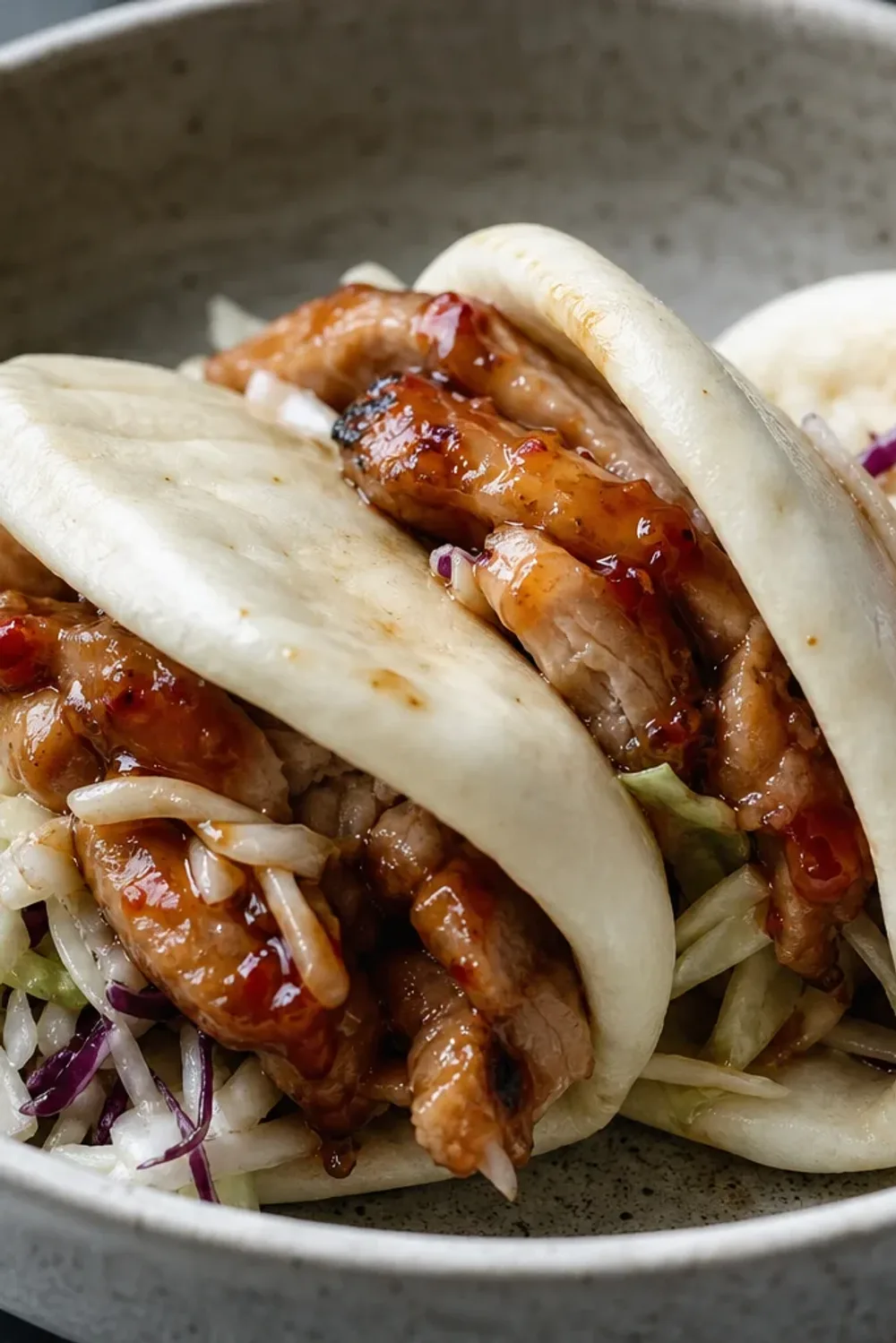 Plated bao sliders filled with sweet chili chicken, topped with vibrant crispy slaw and served on a wooden board.
