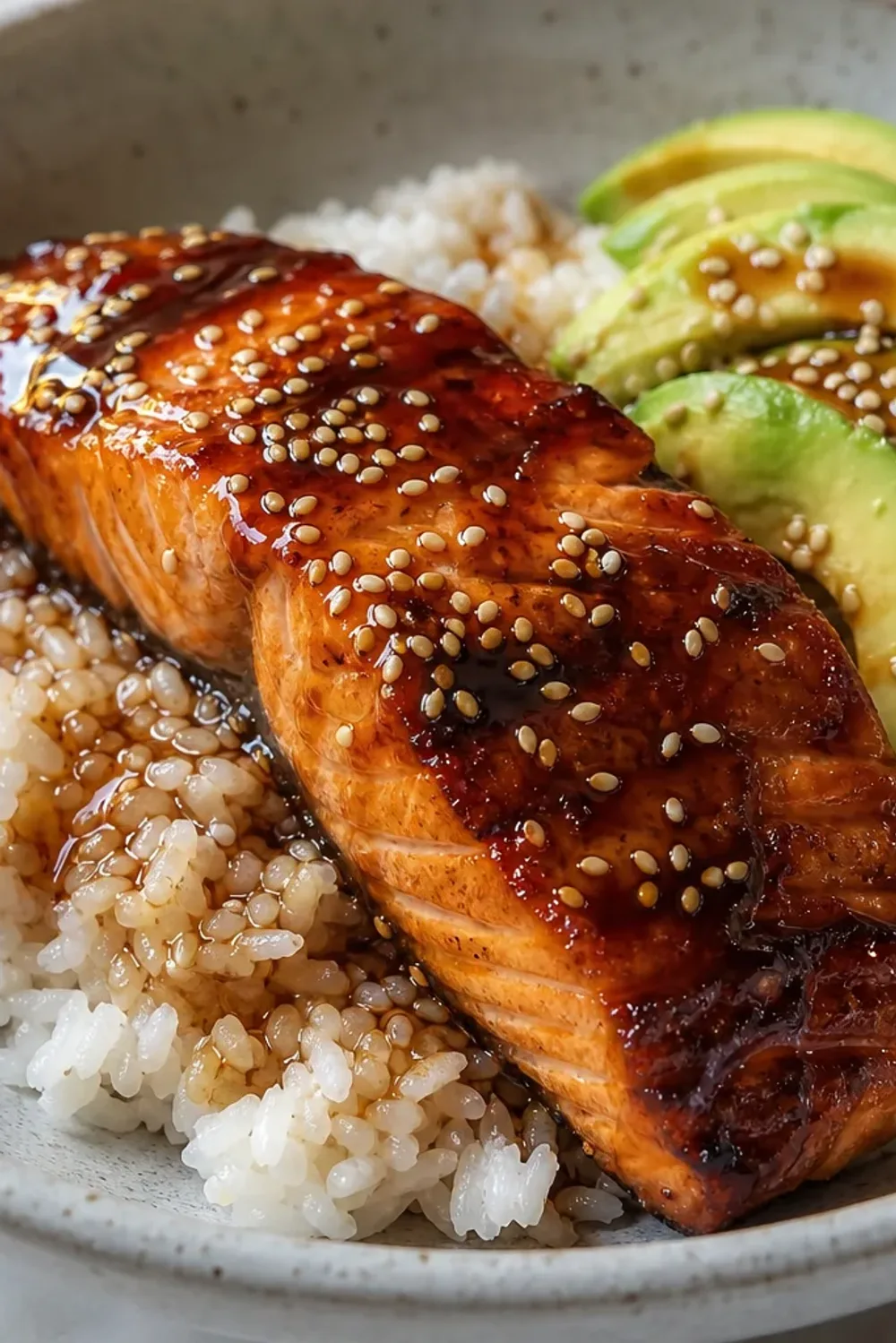 A vibrant rice bowl featuring teriyaki salmon, creamy avocado, and sesame seeds, garnished with green onions.