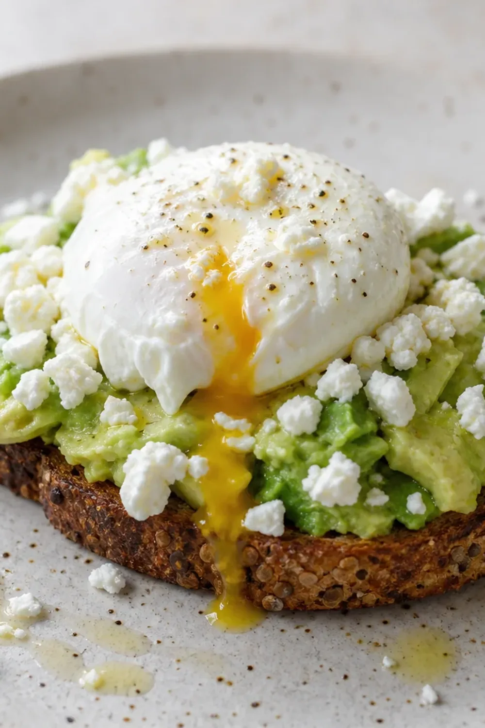 Creamy avocado spread on toasted bread topped with a poached egg and crumbled feta.