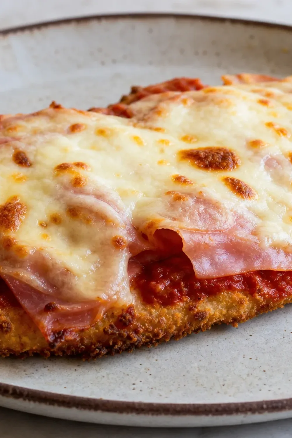 Golden brown chicken breast topped with ham and melted cheese, served with a side of salad.