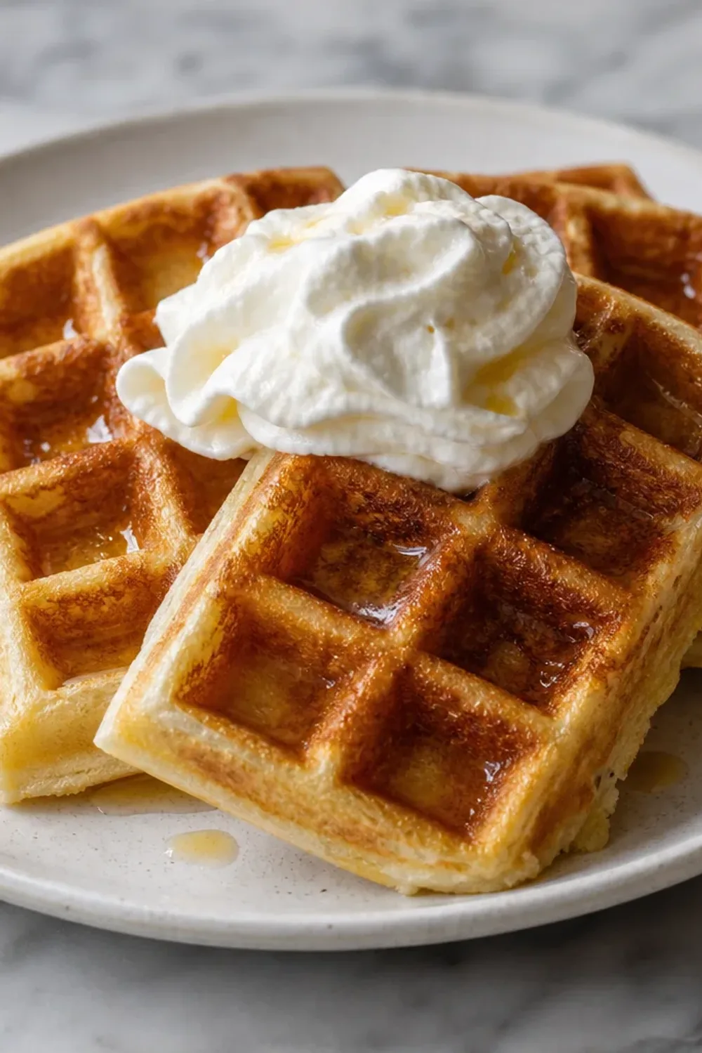 Fluffy Belgian waffles topped with mixed berries and a dollop of whipped cream on a white plate.