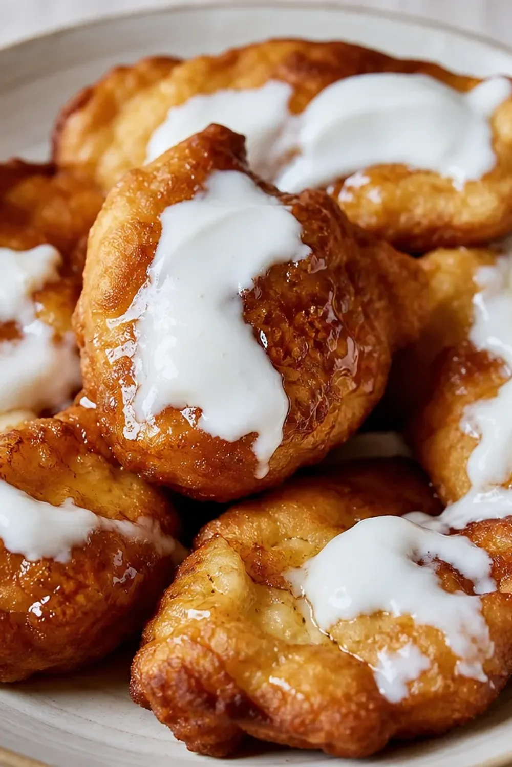 Golden-brown fried dough pastries topped with yogurt and honey drizzle, served on a plate.