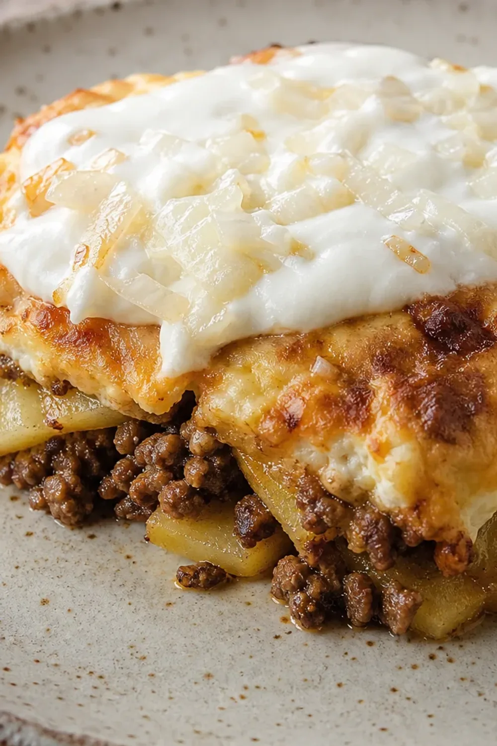 Layered moussaka with golden potatoes, minced meat, and creamy yogurt topping, served in a rustic dish.