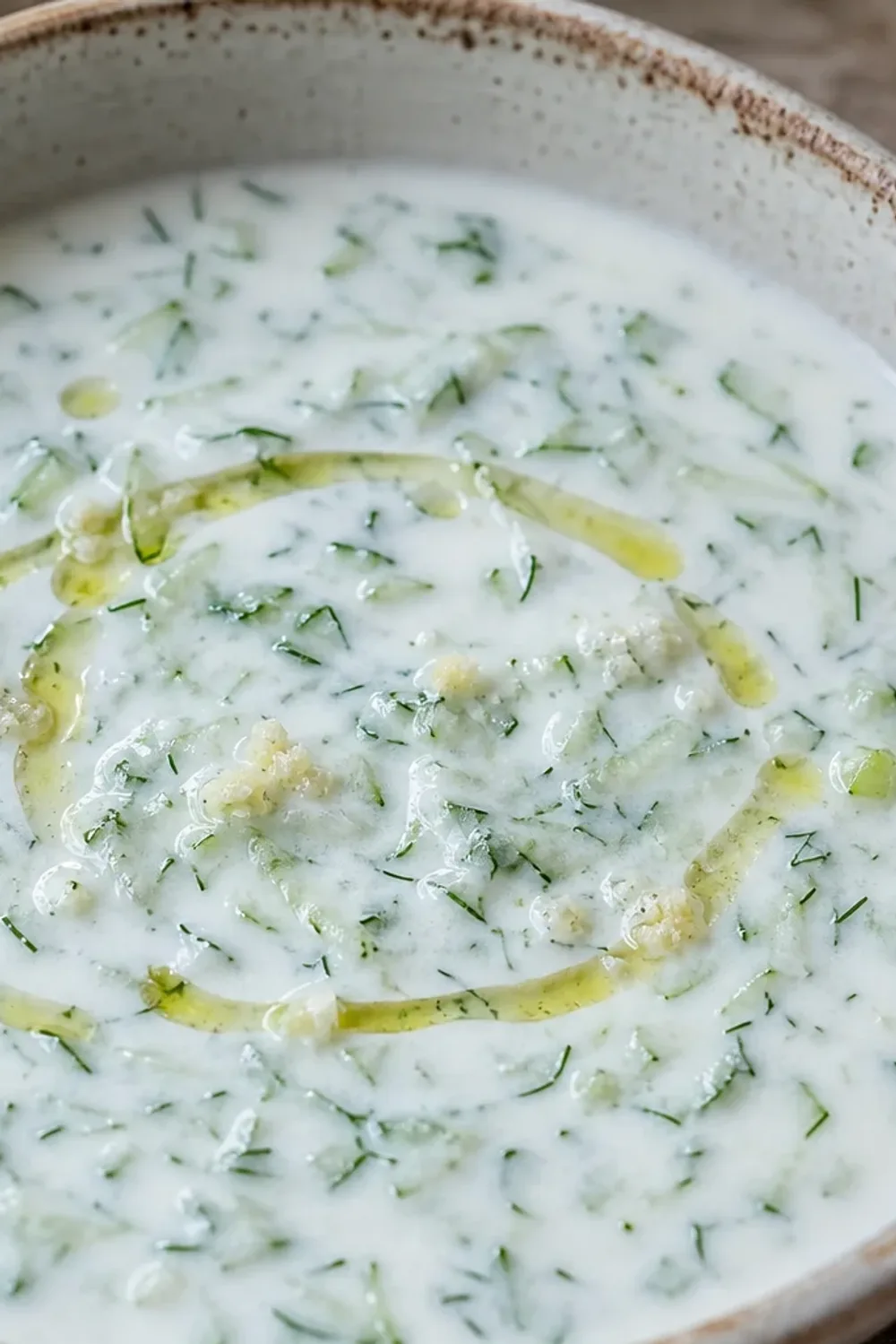 Chilled soup with creamy yogurt, diced cucumbers, and fresh dill garnish in a bowl.
