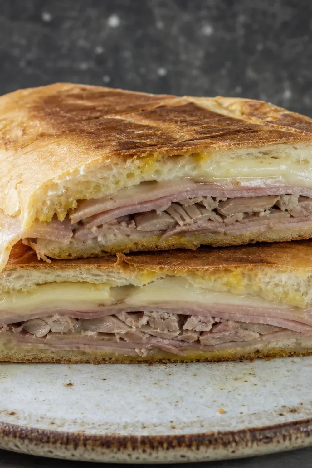 Toasted Cuban sandwich with layers of ham, roast pork, and melted Swiss cheese, golden brown crust.