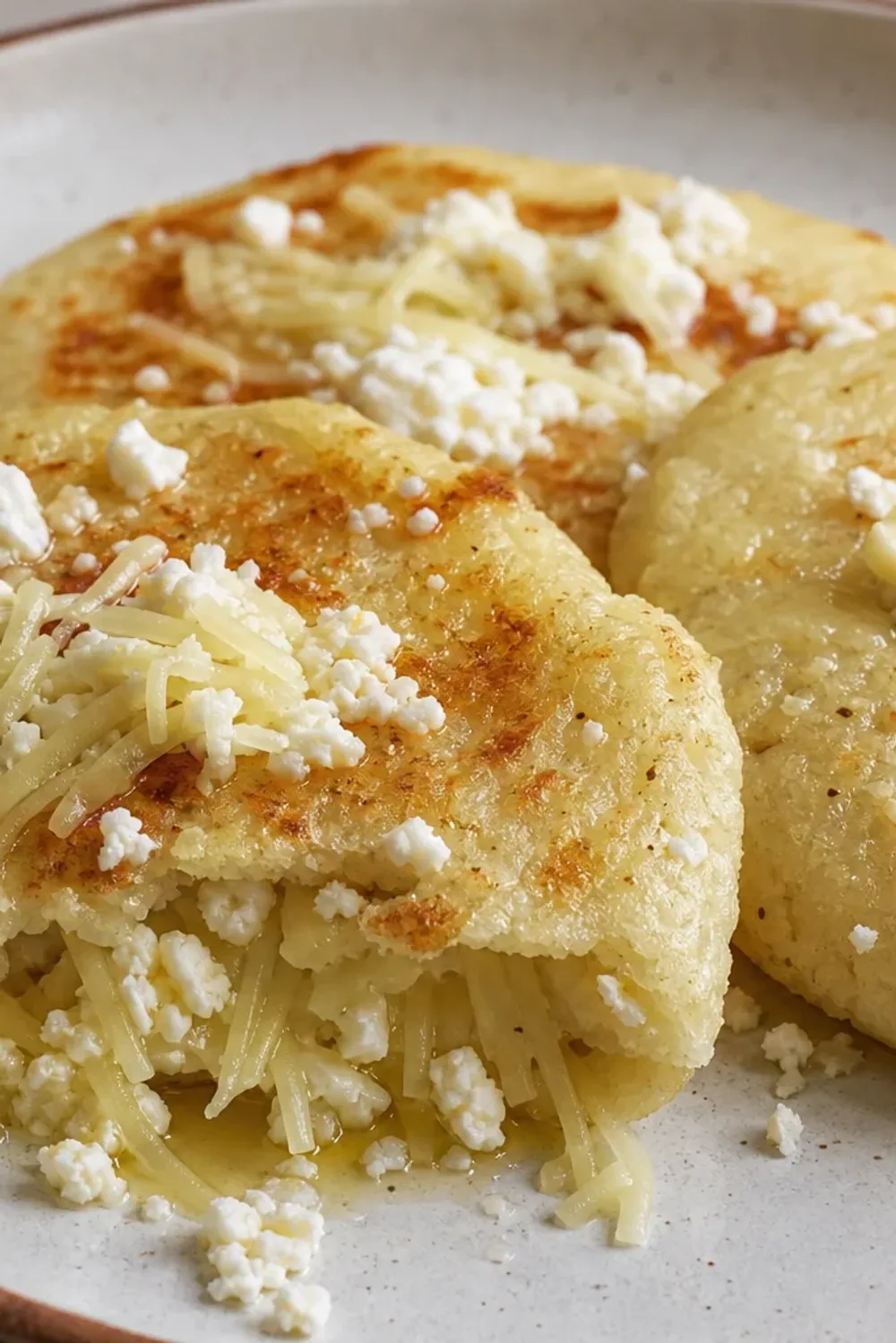 Golden brown arepas filled with melted cheese, garnished on a plate.