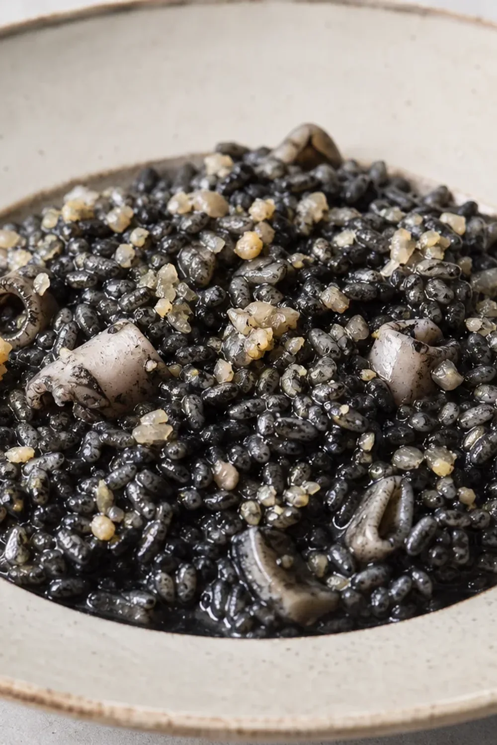 Plated black risotto garnished with cuttlefish, squid ink, and herbs.