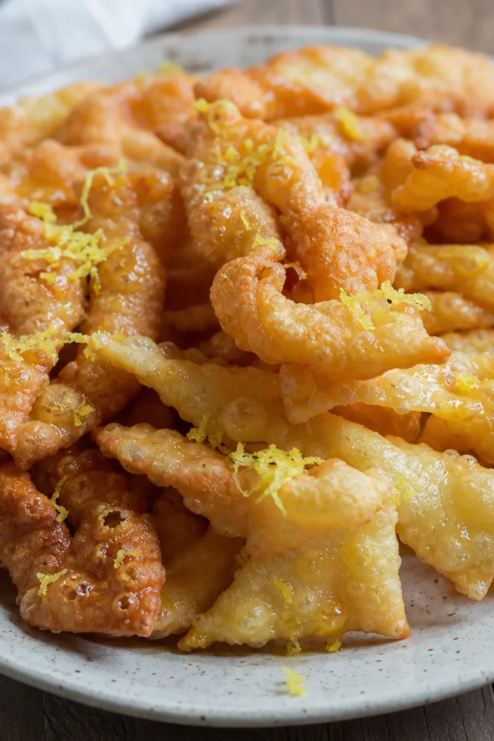 Crispy kroštule pastries dusted with sugar and lemon zest, beautifully arranged on a plate.
