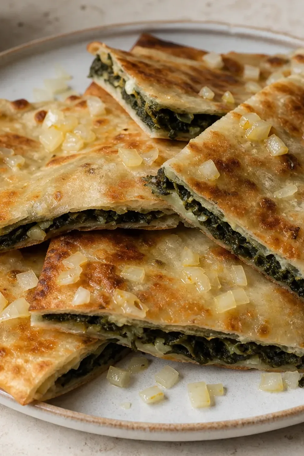 Golden-brown soparnik pastry filled with vibrant green Swiss chard, drizzled with olive oil and cut into squares on a rustic plate.