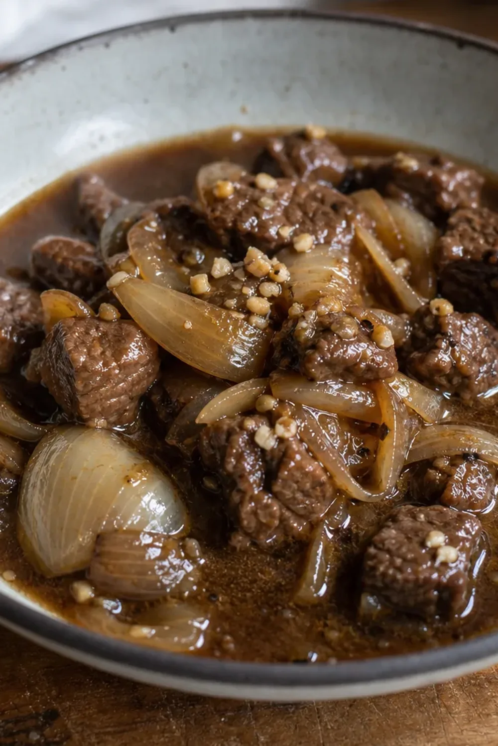 Rich beef and onion stew garnished with fresh herbs in a rustic bowl.