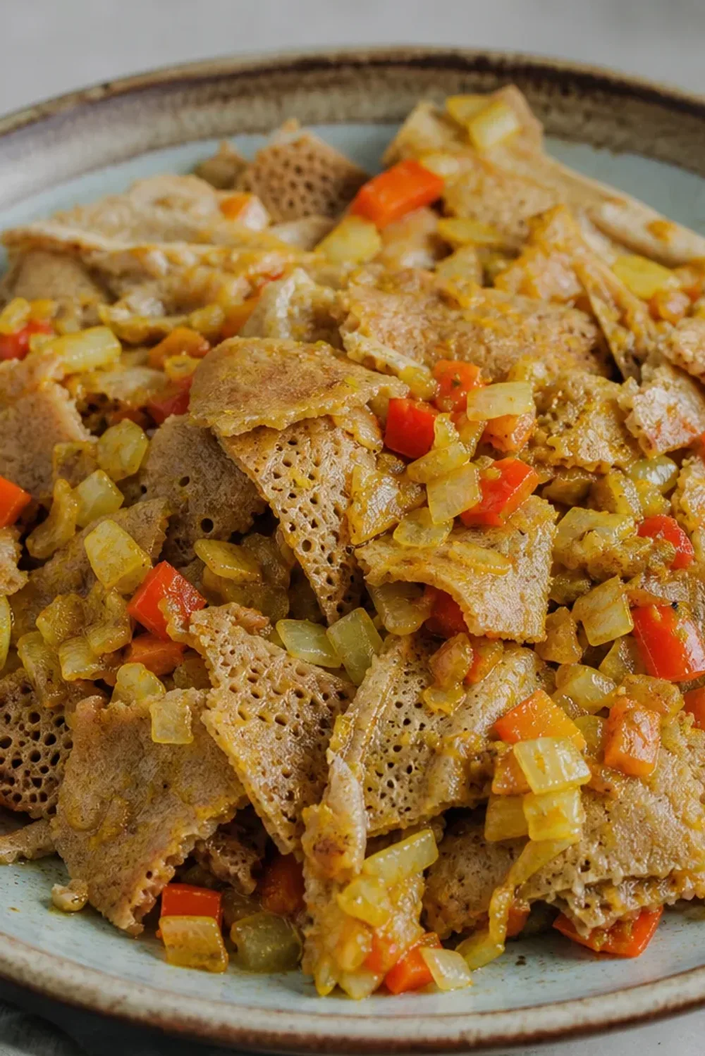 Bowl of Ethiopian Firfir with torn injera, spiced sauce, and fresh herbs garnishing the top.