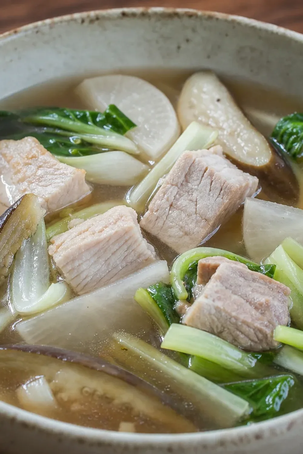 A bowl of sinigang soup featuring tender pork, vibrant vegetables, and a tangy broth, garnished with fresh herbs.