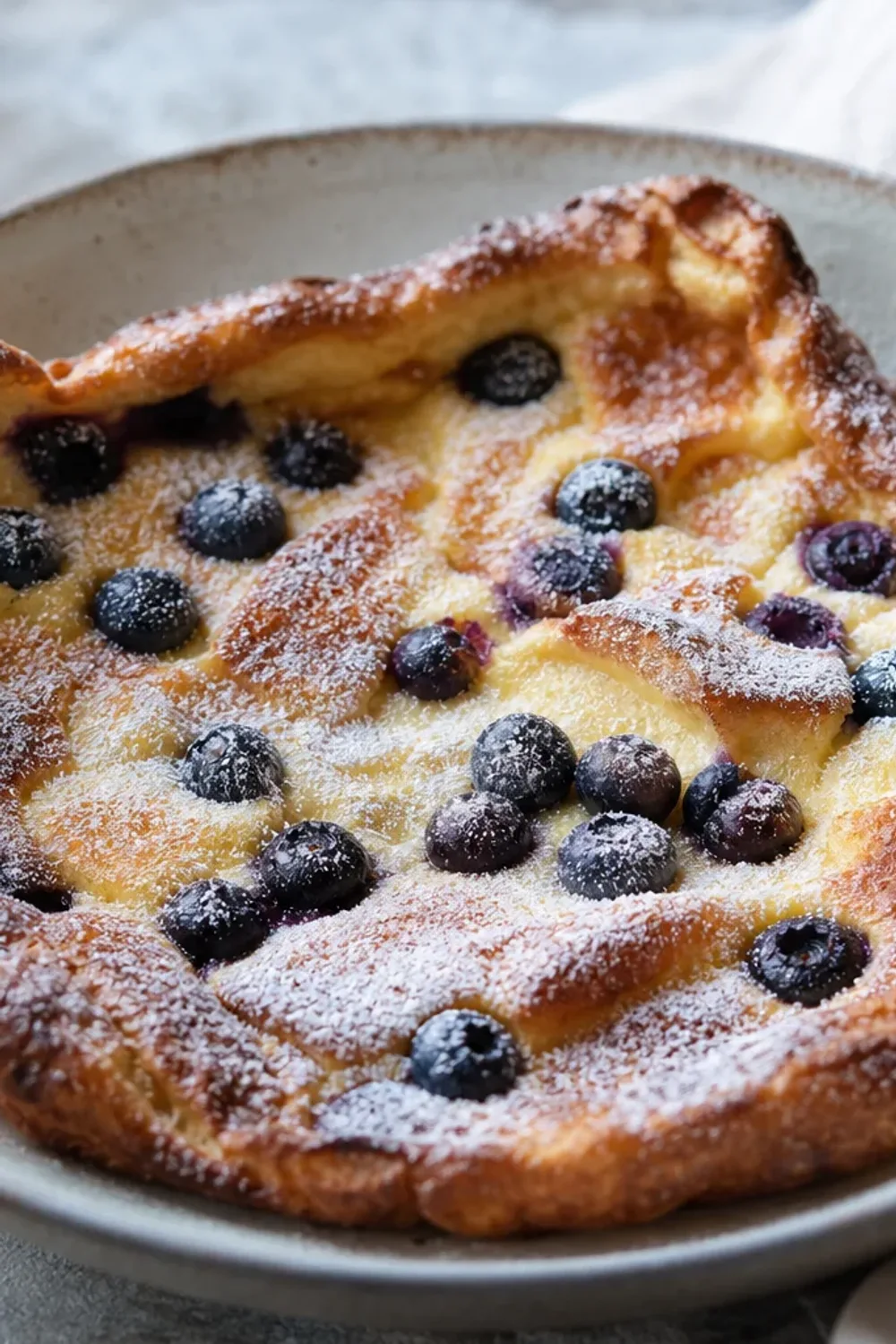 Fluffy Finnish oven pancake topped with assorted fresh berries and powdered sugar, served on a white plate.