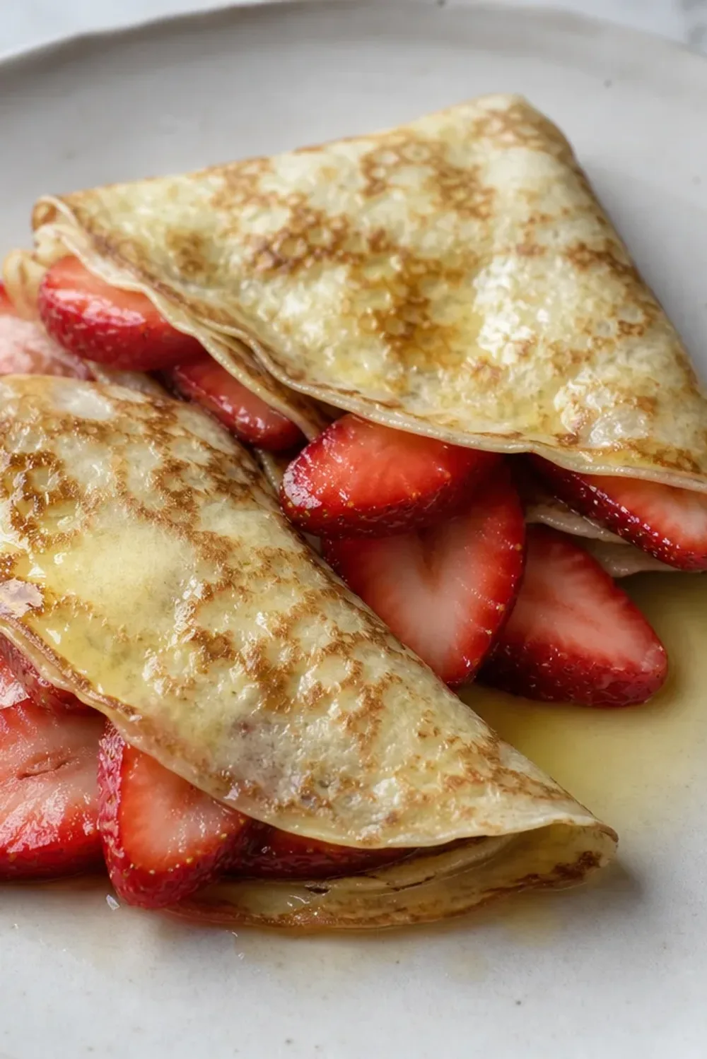 Thin crêpes folded and topped with fresh strawberries and whipped cream, garnished elegantly.