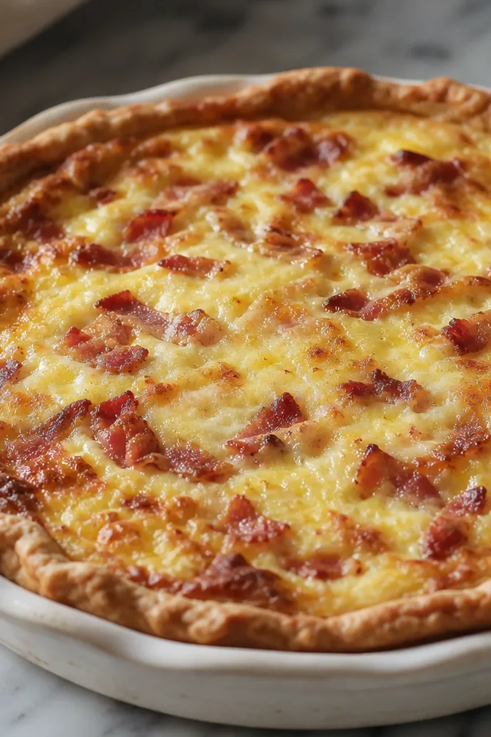 Golden-brown quiche with crispy bacon, melted Gruyère, and a flaky crust on a white plate.