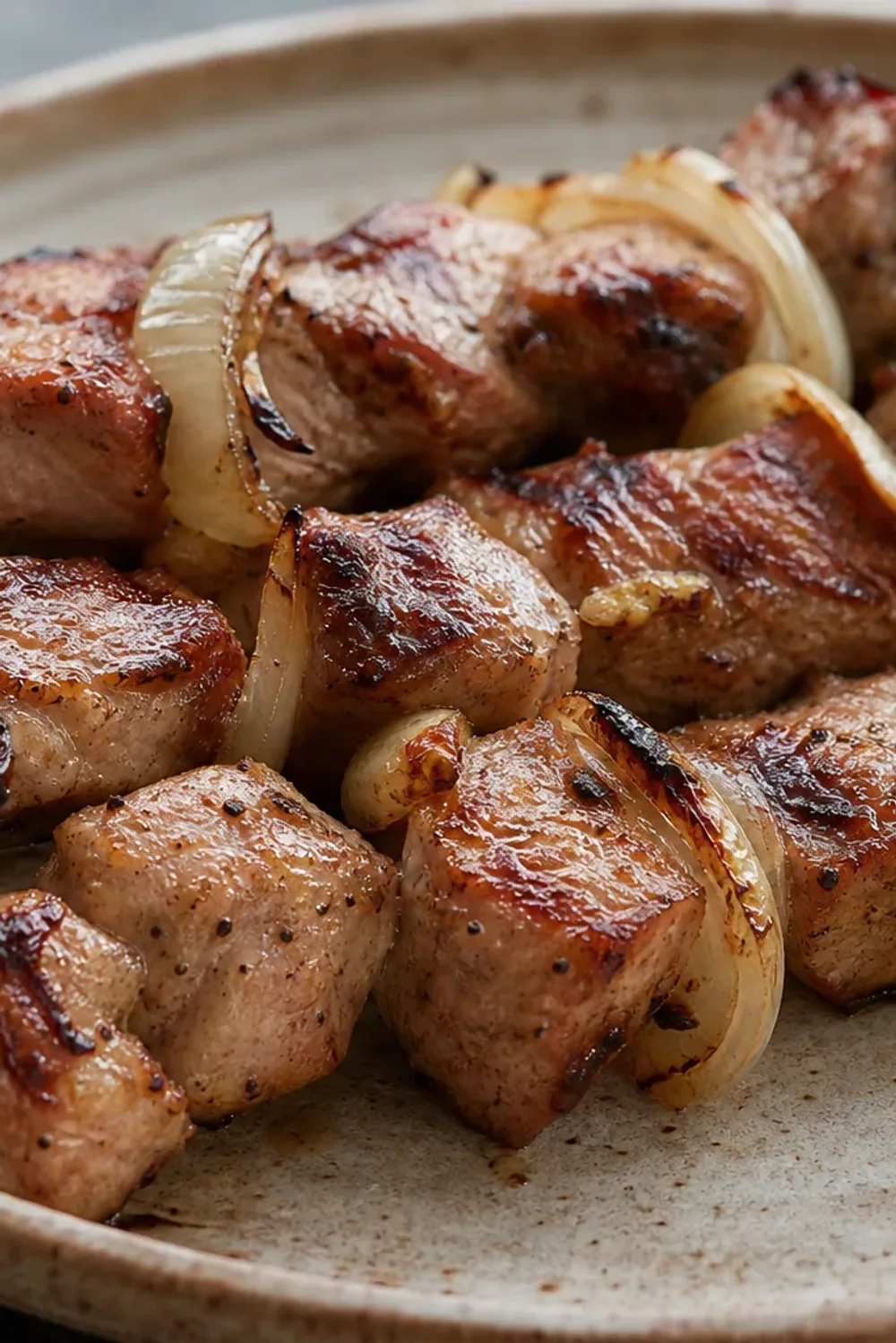 Grilled mtsvadi skewers with juicy marinated meat and caramelized onions, served on a rustic platter.