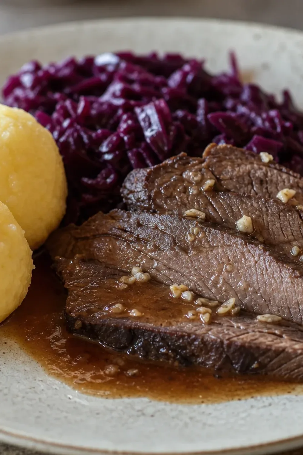 Plated German Sauerbraten with tender meat, vibrant red cabbage, and fluffy potato dumplings garnished with herbs.