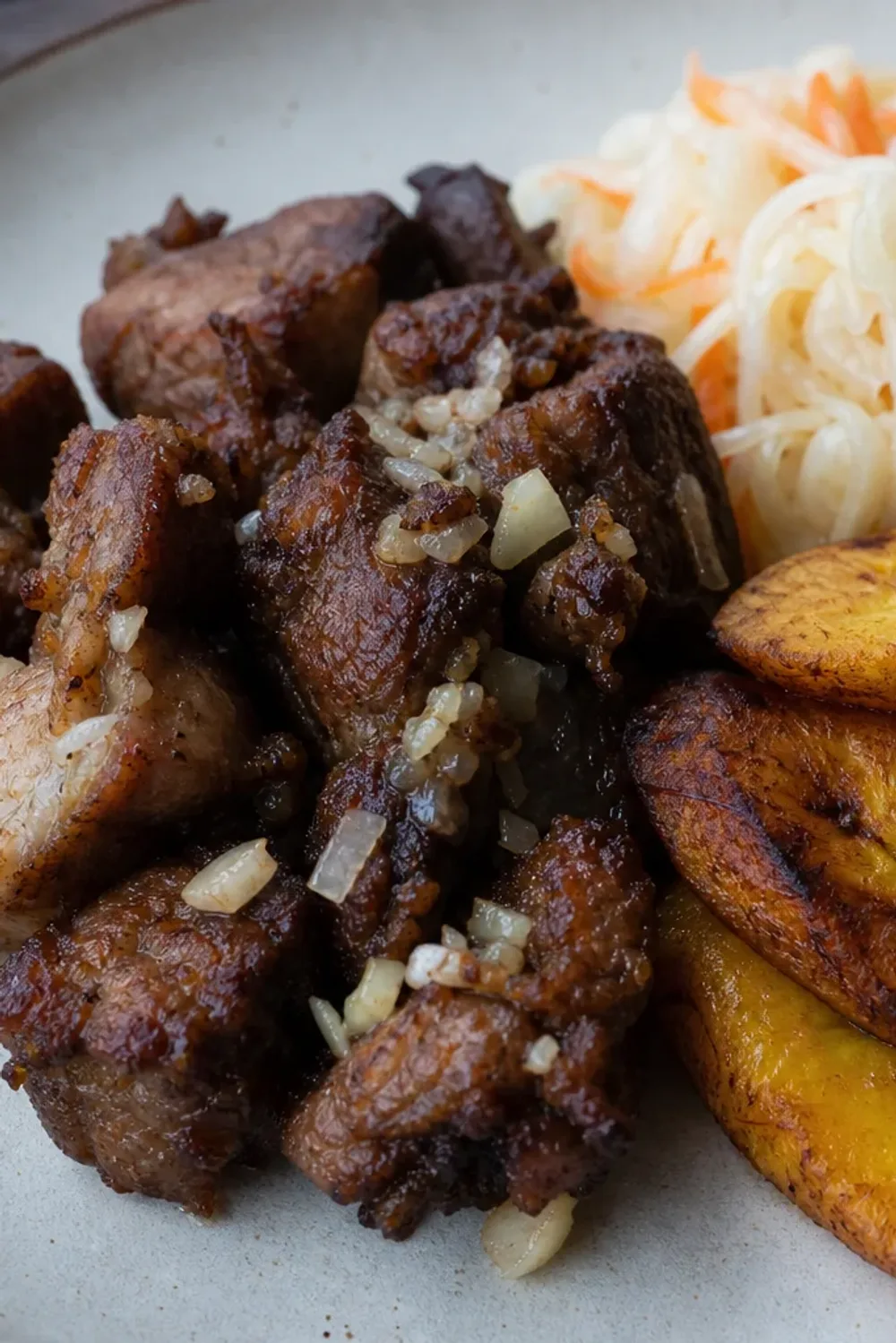 Plated Haitian Griot with vibrant Pikliz and golden fried plantains, showcasing rich flavors and textures.