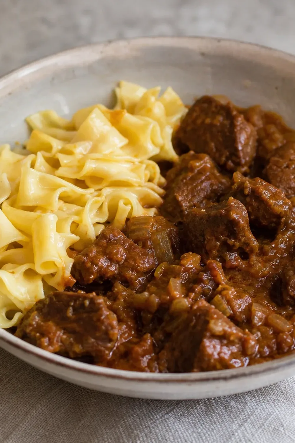 Rich beef pörkölt stew served over smooth egg noodles, garnished with fresh parsley.