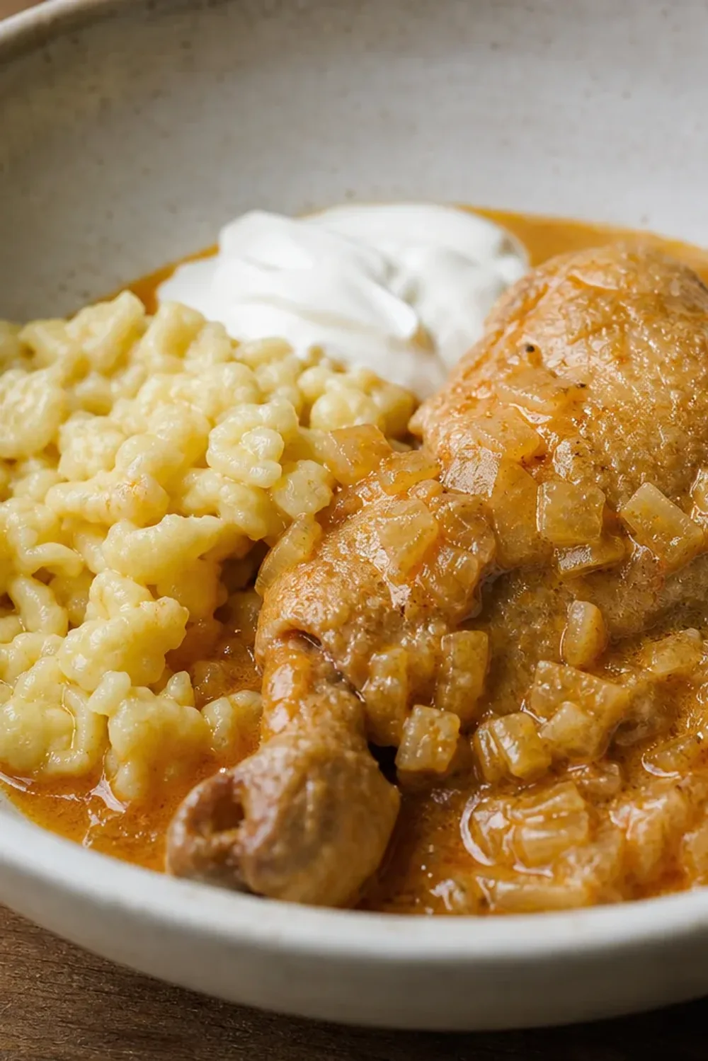 Creamy chicken paprikash with vibrant paprika sauce and soft nokedli dumplings, garnished with parsley.