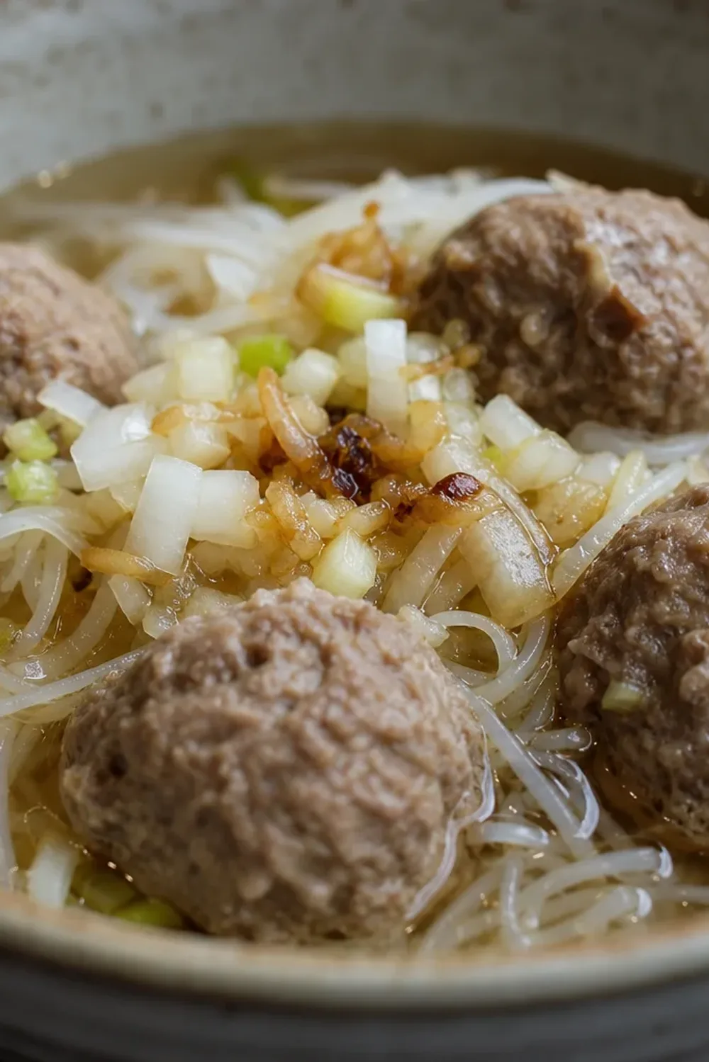 Bowl of Indonesian beef bakso soup with meatballs, noodles, and herbs garnished on top.