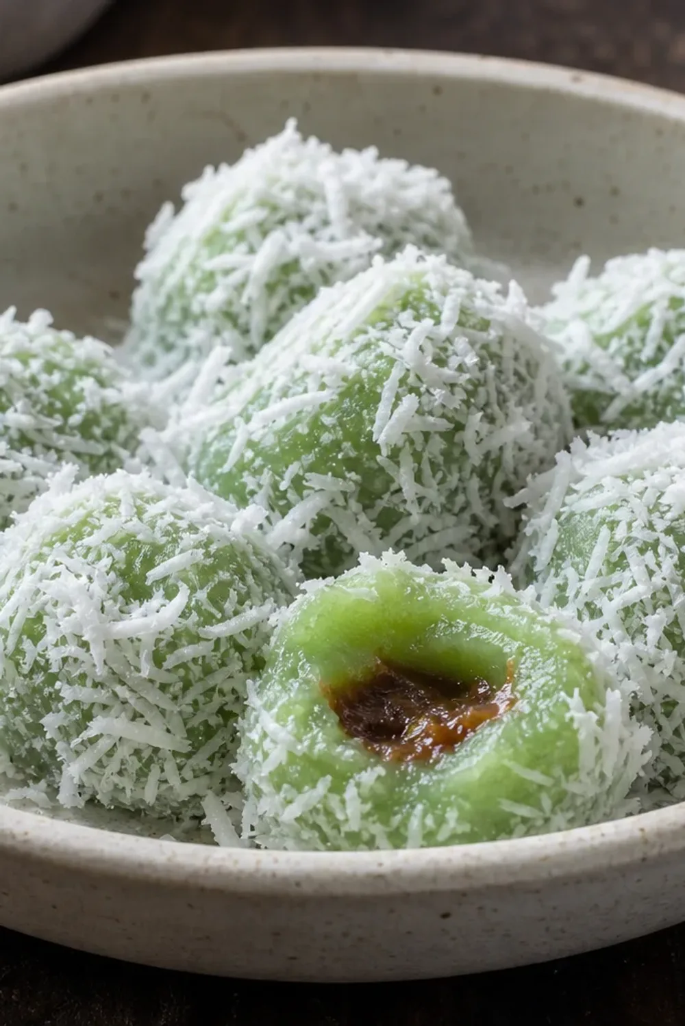 Chewy green rice cakes coated in grated coconut, showcasing palm sugar filling.