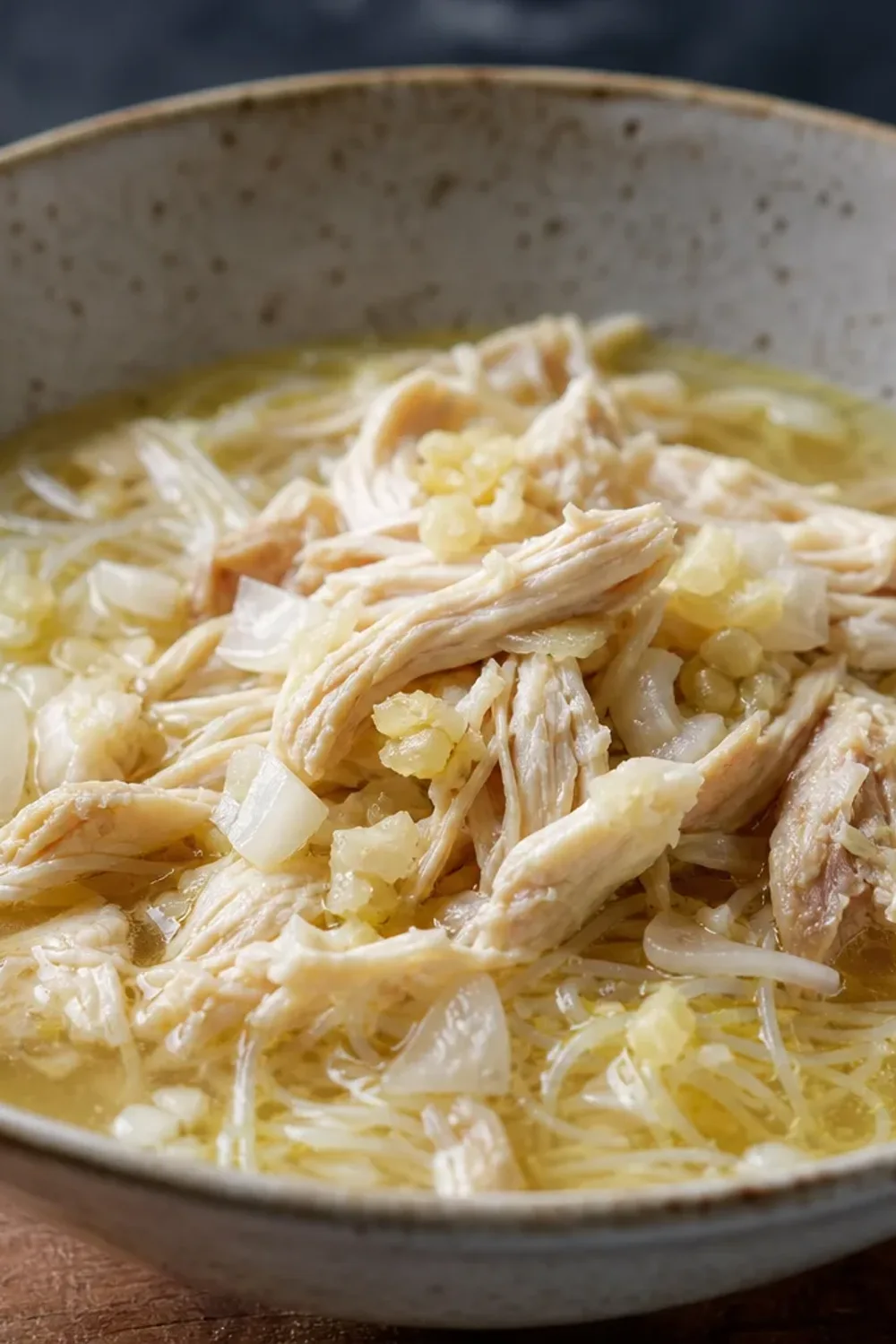 Bowl of Soto Ayam with chicken pieces, vermicelli noodles, and herbs garnished on top.