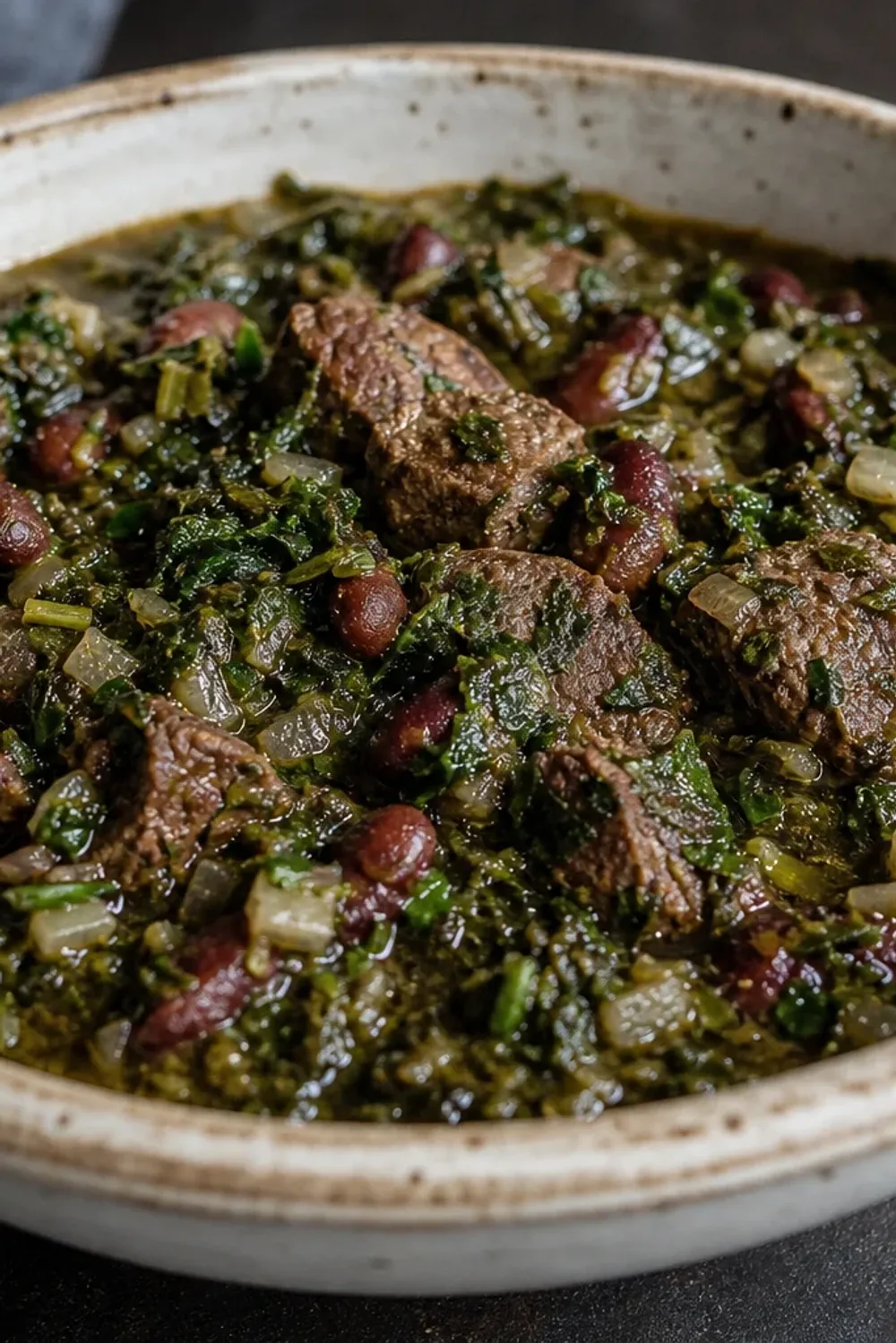 A hearty bowl of Ghormeh Sabzi with tender beef, kidney beans, and vibrant herbs garnished with a slice of lime.
