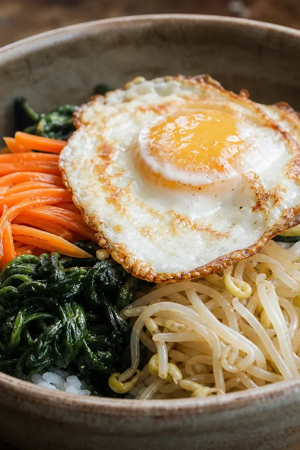 Colorful bibimbap bowl with sautéed vegetables, fried egg, and rice garnished with sesame seeds.