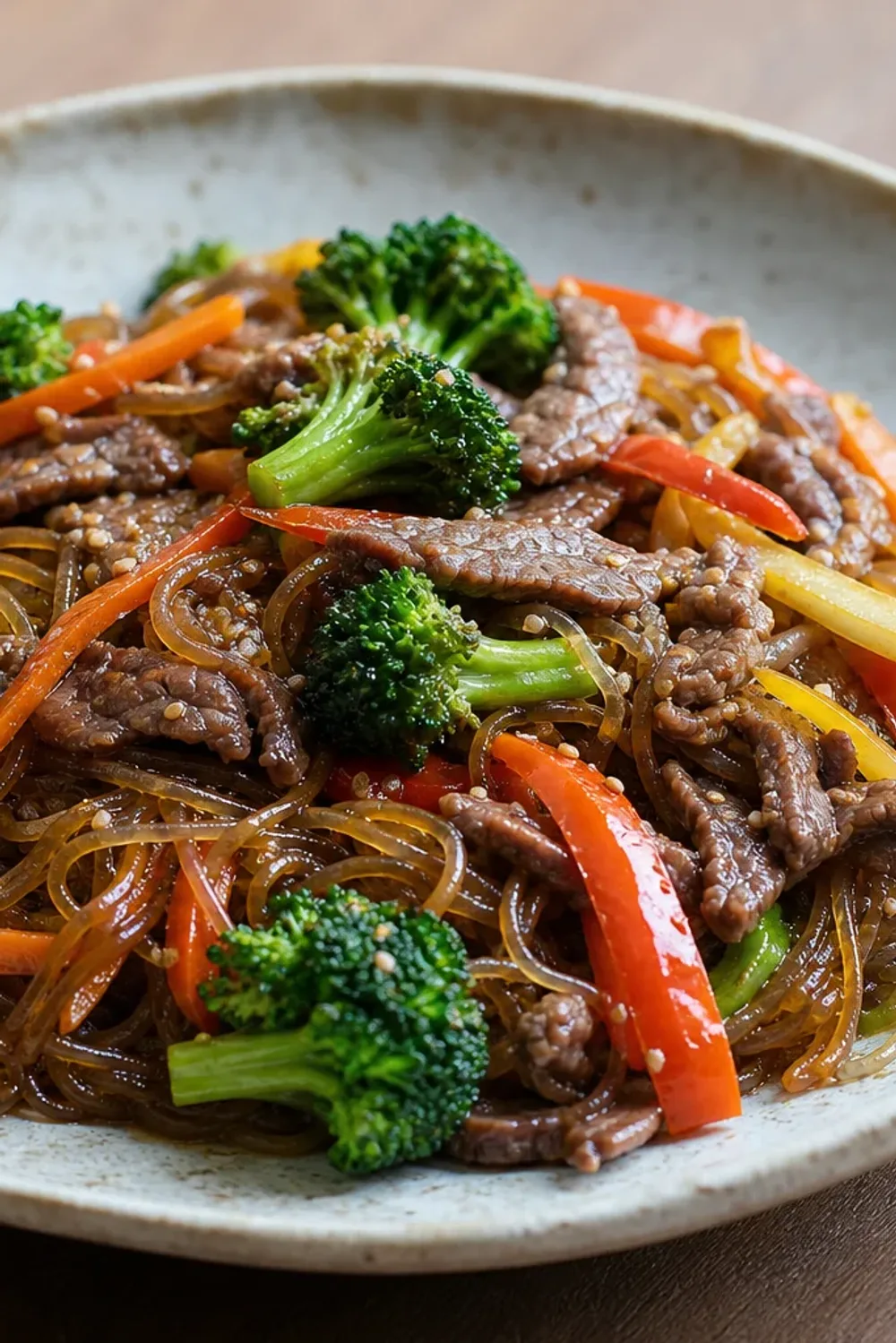 Colorful stir-fried glass noodles with beef and assorted vegetables on a plate.