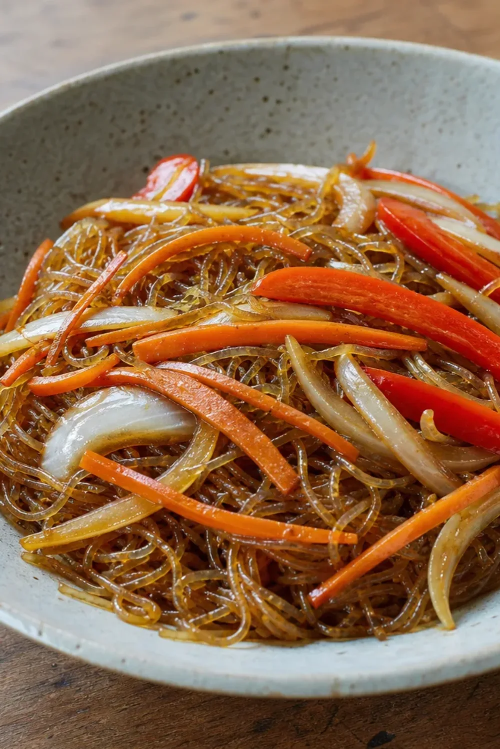 Colorful stir-fried glass noodles with vegetables garnished in a bowl.
