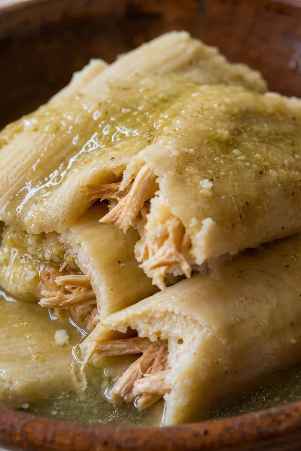 Plated tamales with green salsa, garnished with cilantro and lime, showcasing the texture of masa and chicken filling.