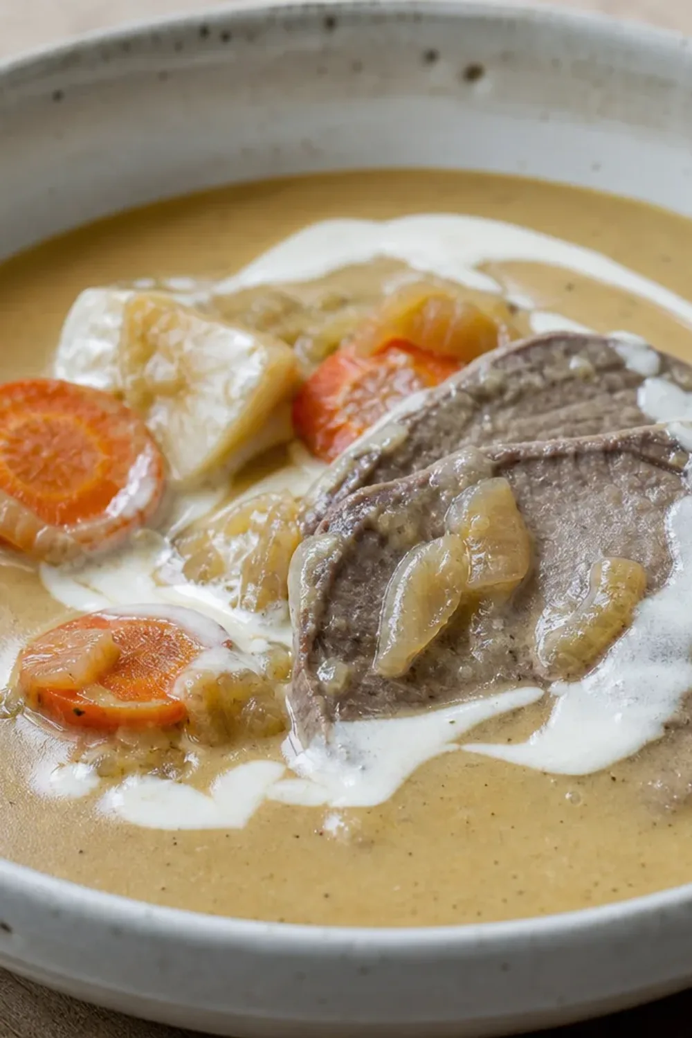 Tender beef sirloin garnished with creamy sauce, served with colorful vegetables on a plate.