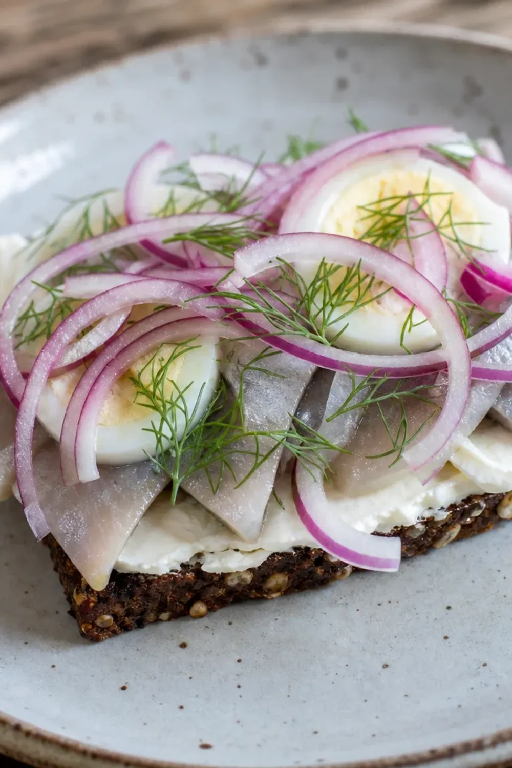 Layers of rye bread topped with herring, egg, and fresh herbs, beautifully presented on a plate.